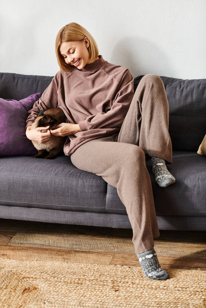 Kobieta z krótkimi włosami relaksująca się na kanapie, trzymająca i głaskająca kota z troską i miłością. - Zdjęcie, obraz