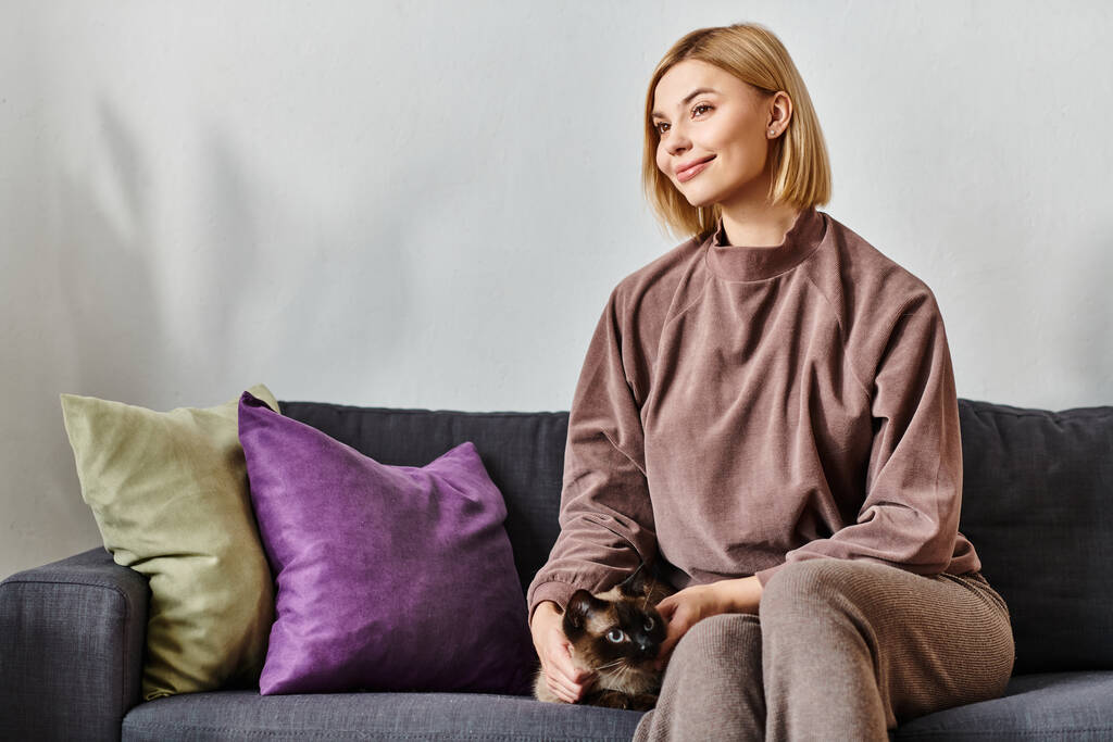 Короткошерста жінка мирно сидить на дивані, зв'язавшись зі своєю кішкою. - Фото, зображення