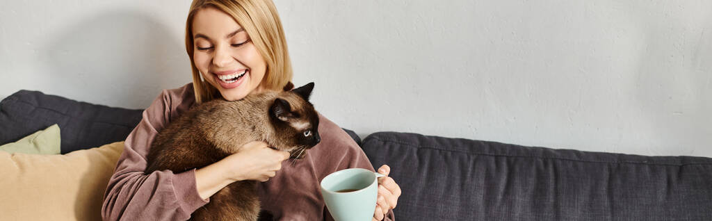 Une femme aux cheveux courts se détend sur un canapé, berçant son chat dans ses bras, profitant d'un moment paisible à la maison. - Photo, image