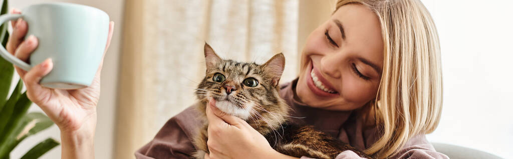 Eine Frau mit kurzen Haaren lächelt, als sie eine Katze in ihren Armen hält, die eine herzerwärmende Verbundenheit zwischen ihnen zeigt. - Foto, Bild