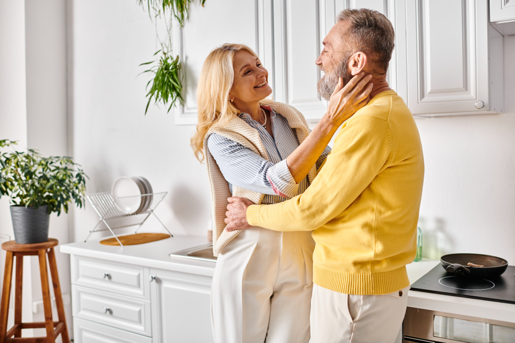 A mature loving couple in cozy homewear standing together in their kitchen, enjoying quality time together. - Photo, Image