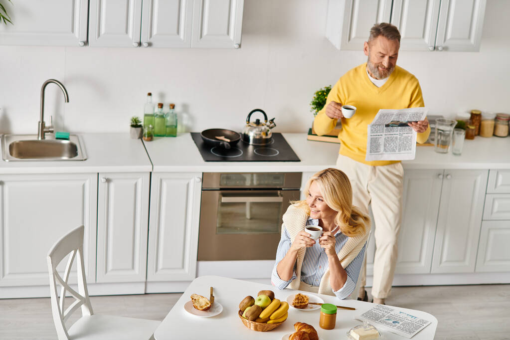Egy érett szerető pár otthonos viseletben élvezi az együtt töltött időt otthon a konyhában, megosztva a nevetést és elkészítve az ételt.. - Fotó, kép