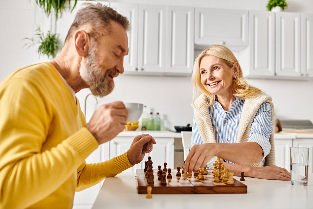 Um homem maduro e uma mulher em trajes acolhedores se envolvem em um jogo de xadrez, profundamente pensados enquanto eles planejam seus próximos movimentos.. - Foto, Imagem
