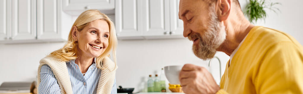 Зрелая любящая пара в уютной домашней одежде проводит время вместе на кухне, готовит и смеется. - Фото, изображение