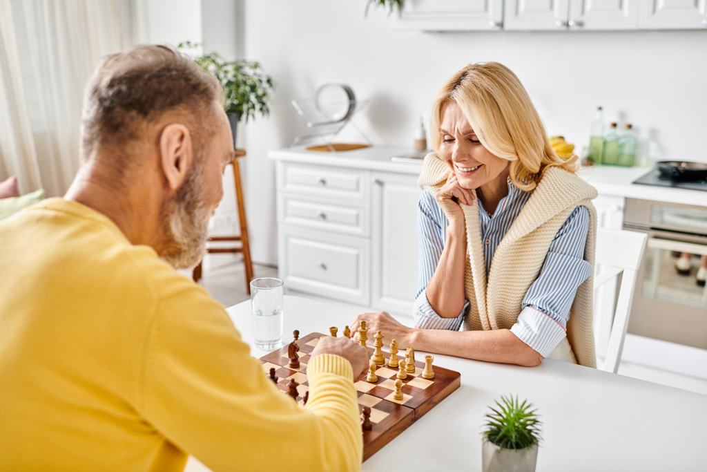 Een volwassen liefdevol paar in gezellige huiskledij die betrokken zijn bij een strategisch schaakspel thuis. - Foto, afbeelding