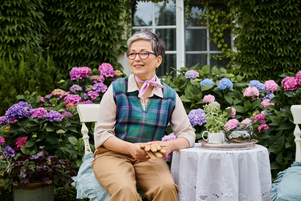 schöne lustige reife Frau sitzt zur Teezeit in der Nähe von Haus in England im Garten und schaut weg - Foto, Bild