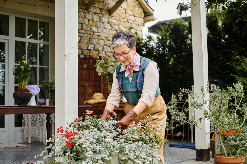 όμορφη κομψή ώριμη γυναίκα με γυαλιά που φροντίζει τα λουλούδια της κοντά στο σπίτι της στην Αγγλία - Φωτογραφία, εικόνα