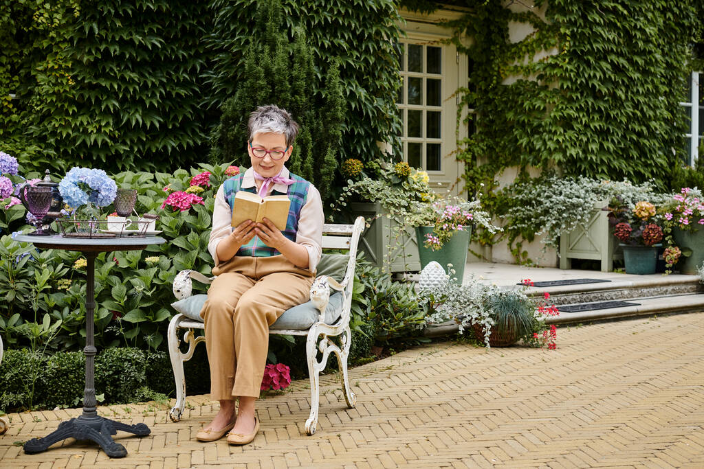tyylikäs kypsä iloinen nainen, jolla on lasit lukeminen teeaikaan lähellä kotiaan Englannin maaseudulla - Valokuva, kuva