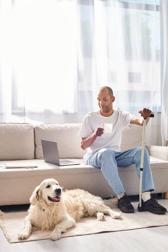 Ein behinderter Afroamerikaner mit Myasthenia gravis sitzt auf einer Couch neben seinem treuen Labrador-Hund. - Foto, Bild