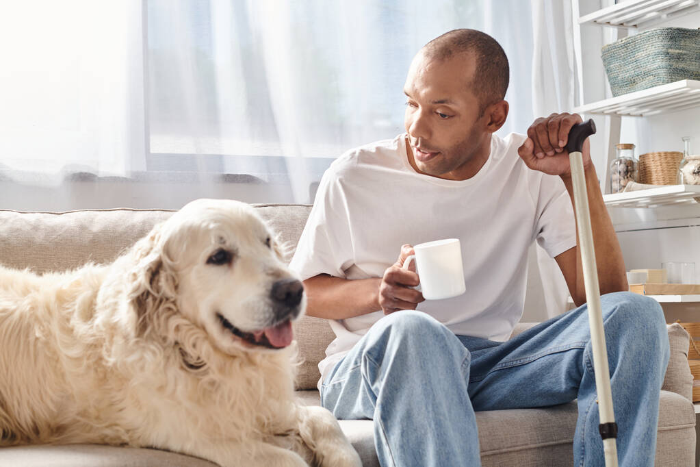 Egy myasthenia gravis-os férfi ül a kanapén, élvezi a társaságát a hűséges labrador kutyájával egy hangulatos nappaliban.. - Fotó, kép