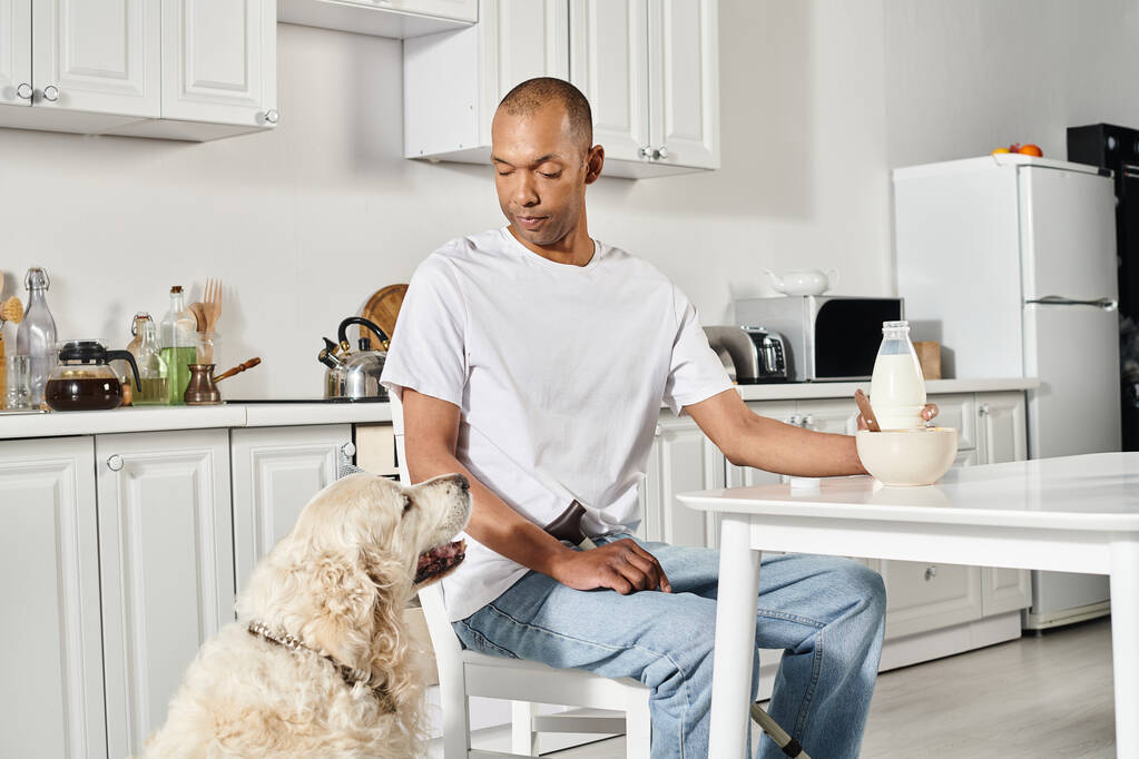 Egy rokkant afro-amerikai férfi ül a konyhaasztalnál hű labrador kutyájával, bemutatva a sokszínűséget és a befogadást.. - Fotó, kép