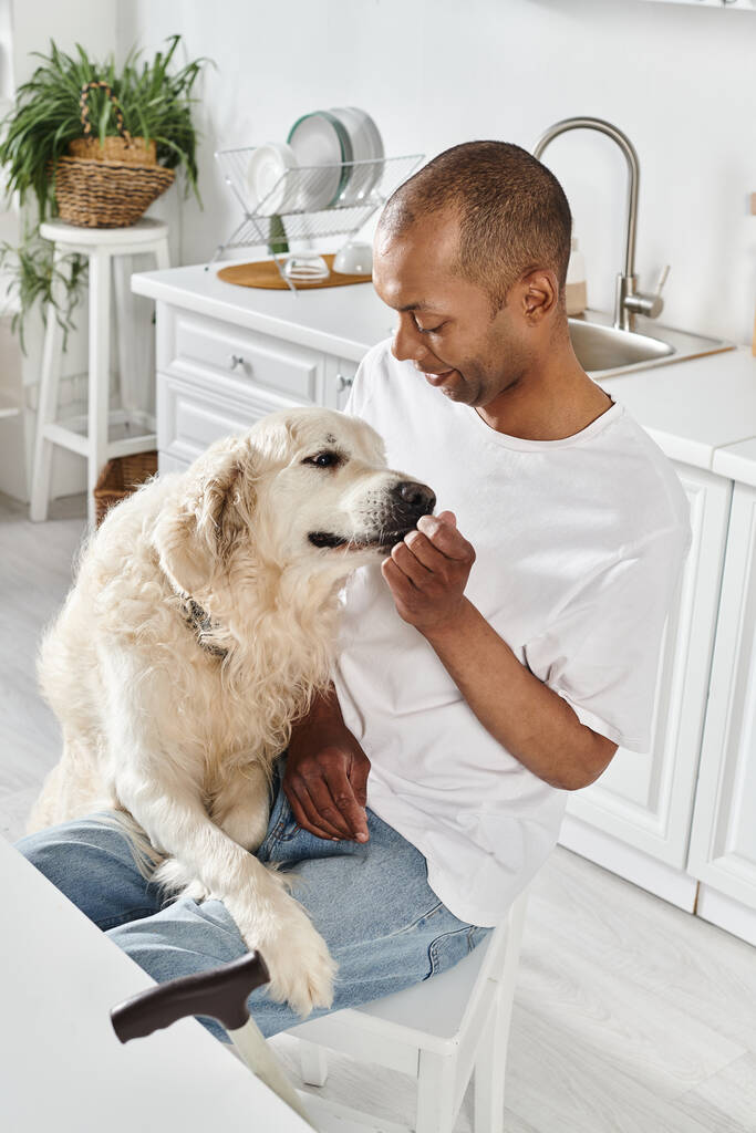 Um homem afro-americano deficiente acaricia amorosamente seu fiel Labrador em um ambiente acolhedor de cozinha, irradiando calor e companheirismo. - Foto, Imagem