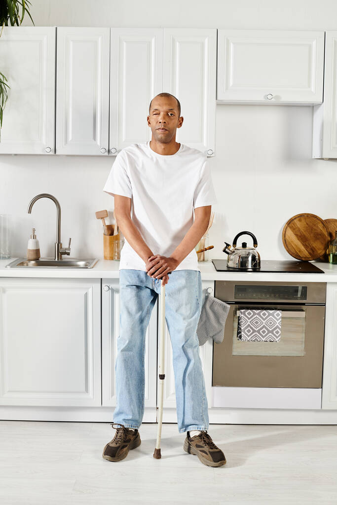 Un Afro-Américain avec une canne se tient en confiance dans une cuisine, montrant force et résilience. - Photo, image