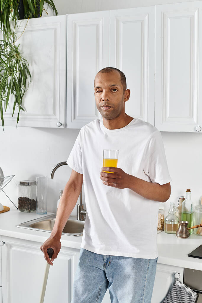 Afroamerykanin z zespołem miastenii stoi w kuchni trzymając szklankę soku pomarańczowego.. - Zdjęcie, obraz