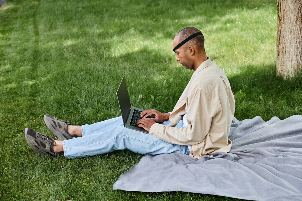 African American man with Myasthenia Gravis in a wheelchair, using a laptop outside on grass - Photo, Image