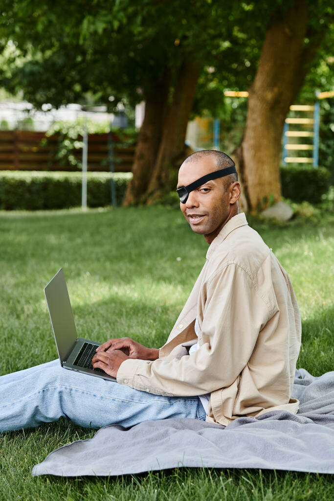 Miyastenia gravis 'i olan bir Afrikalı Amerikalı çimlerin üzerinde otururken dizüstü bilgisayar kullanıyor. - Fotoğraf, Görsel