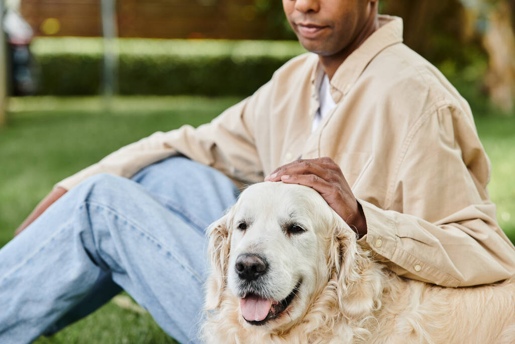 Un hombre con síndrome de miastenia gravis pacíficamente se sienta en la hierba con su leal perro Labrador a su lado. - Foto, Imagen