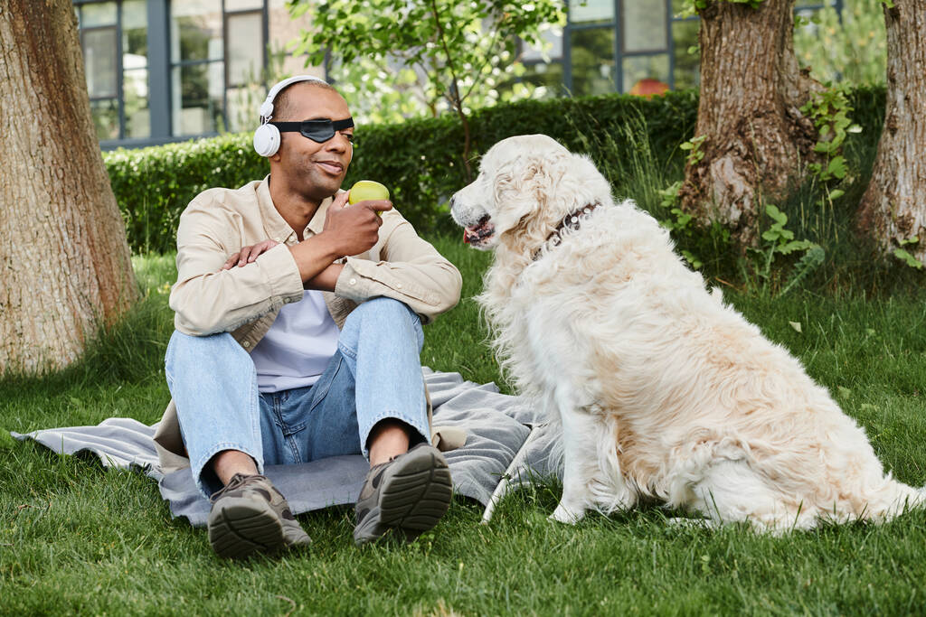 Miyastenia gravis sendromlu, özürlü bir Afrikalı Amerikalı, çimenlerin üzerinde dost bir Labrador köpeğinin yanında oturuyor.. - Fotoğraf, Görsel