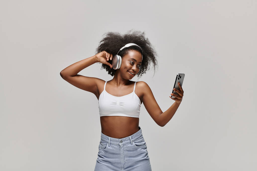 Μια εκπληκτική Αφρο-Αμερικανίδα με λευκό μπλουζάκι κρατάει κομψά ένα κινητό τηλέφωνο.. - Φωτογραφία, εικόνα