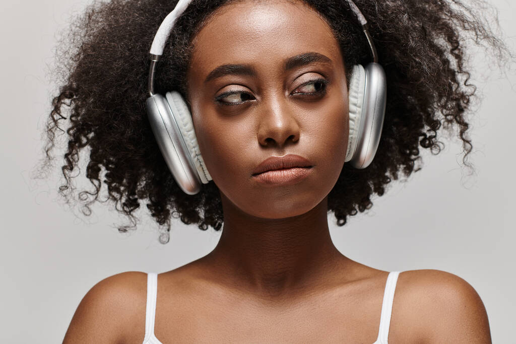 Молодая афроамериканка с вьющимися волосами слушает музыку через наушники. - Фото, изображение