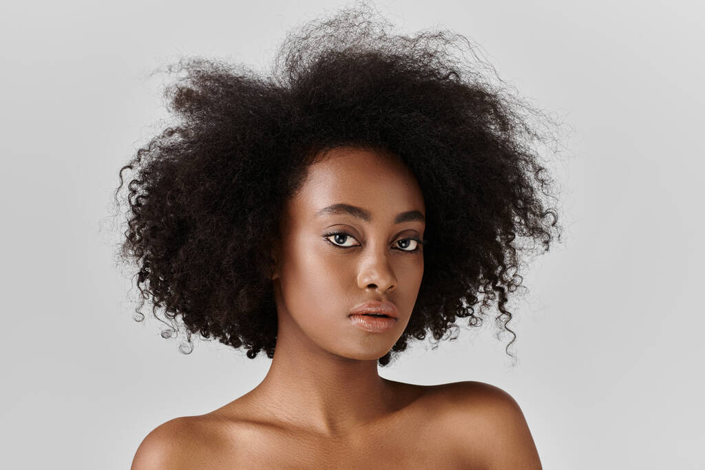 Μια νεαρή Αφροαμερικανή με σγουρά μαλλιά ποζάρει σε στούντιο.. - Φωτογραφία, εικόνα