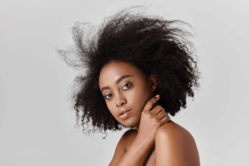 Una hermosa joven afroamericana con el pelo rizado posando para un retrato con su pelo brillante en exhibición. - Foto, imagen