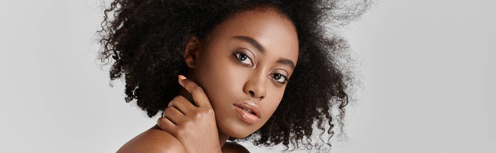 Uma jovem mulher afro-americana deslumbrante com cabelo encaracolado atinge uma pose em um estúdio. - Foto, Imagem