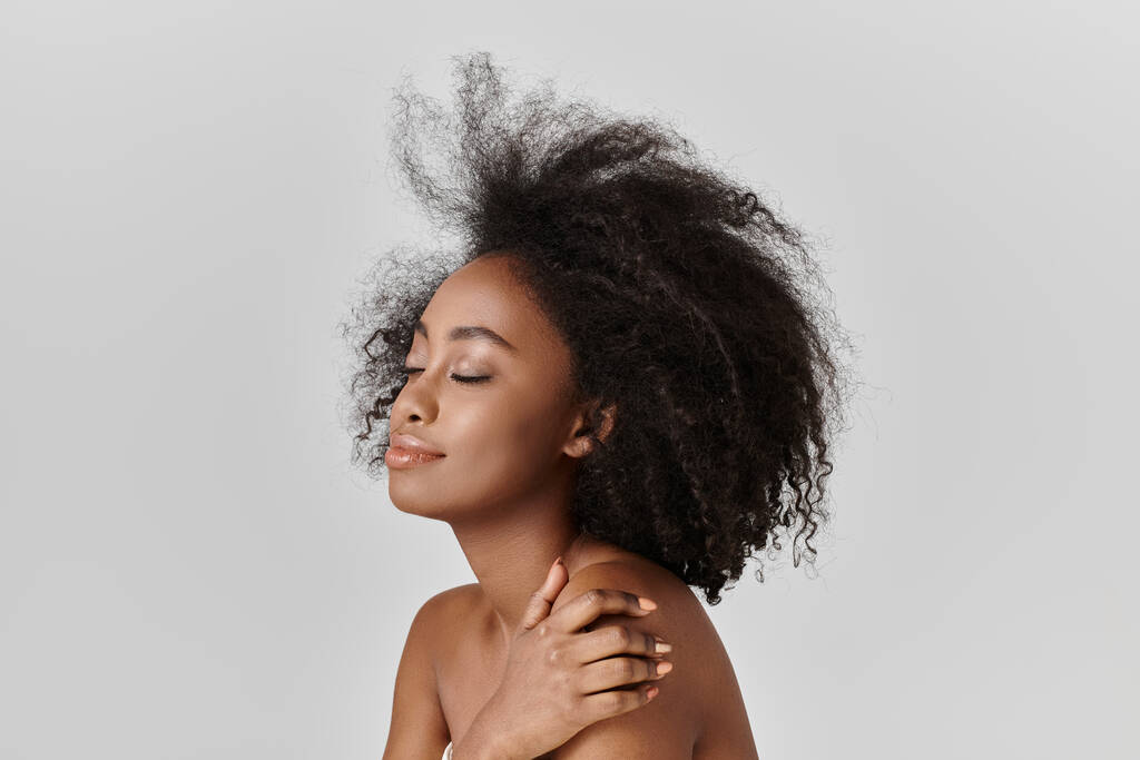 Una hermosa joven afroamericana con el pelo rizado está desnuda mientras su cabello cae en cascada en el viento, exudando gracia y belleza. - Foto, imagen