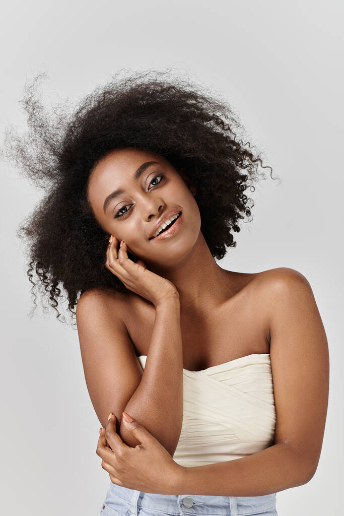 Uma mulher afro-americana deslumbrante com um penteado afro encaracolado posando para a câmera em um estúdio. - Foto, Imagem