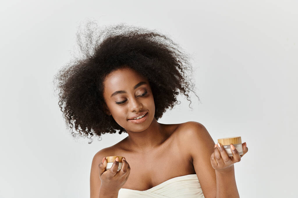 Een betoverende jonge Afro-Amerikaanse vrouw met krullend haar met een crème pot - Foto, afbeelding