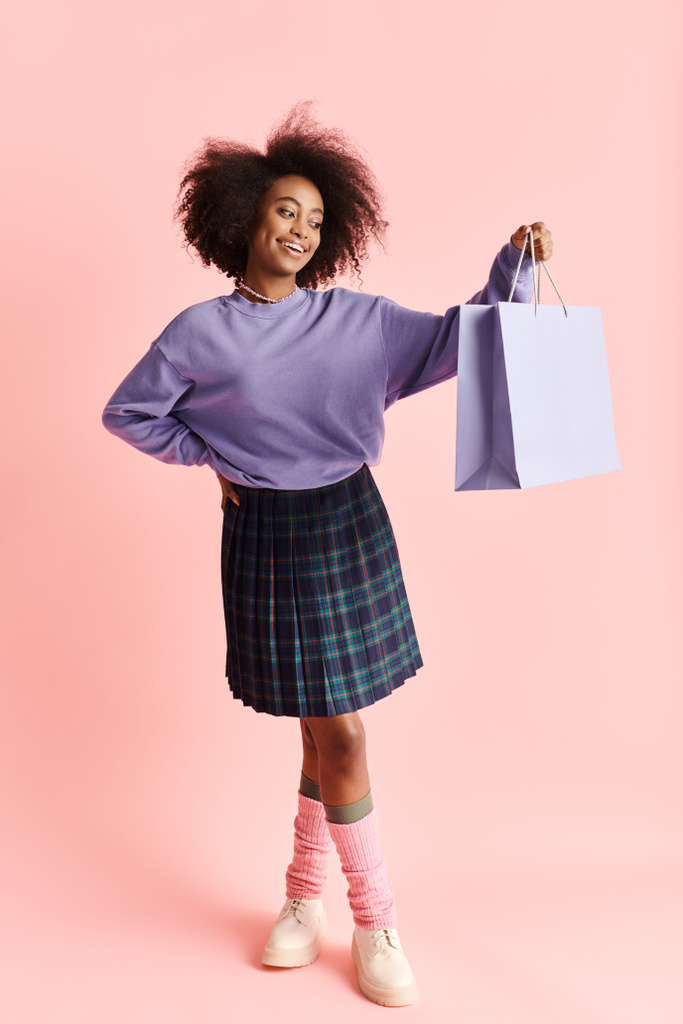 Egy fiatal afro-amerikai nő göndör hajjal mosolyog, miközben egy bevásárlószatyrot tart a kezében.. - Fotó, kép