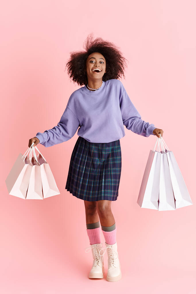Afroamerykanka z kręconymi włosami, ubrana w spódnicę, trzymająca torby na zakupy w stylowej pozie. - Zdjęcie, obraz