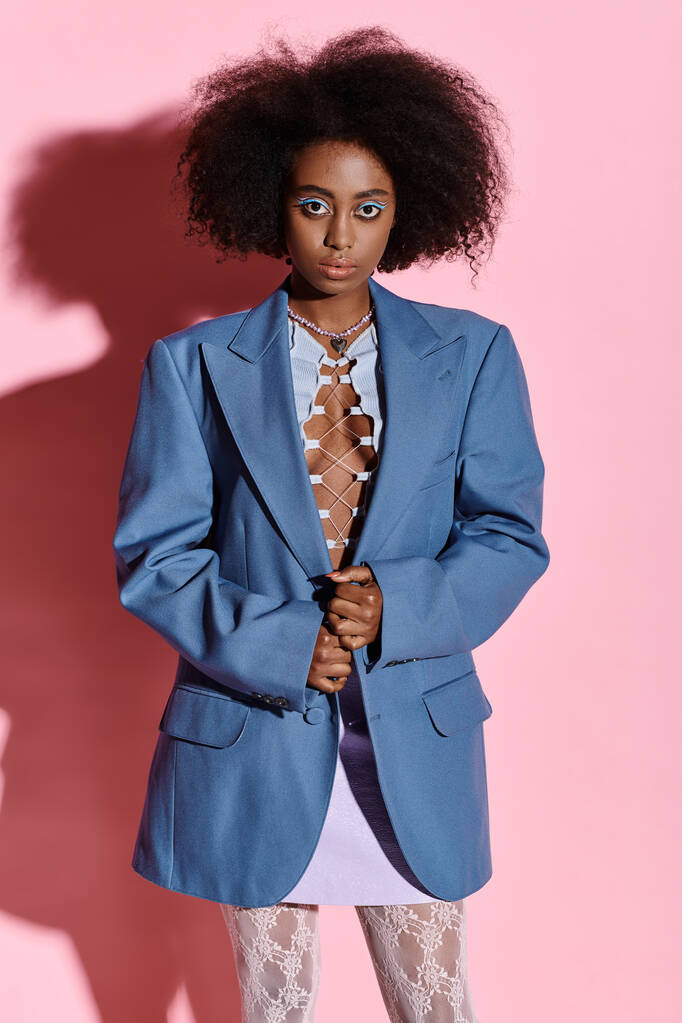 StyFfsish African American woman with curly hair posing confidently in a blue jacket and white pants. - Photo, Image