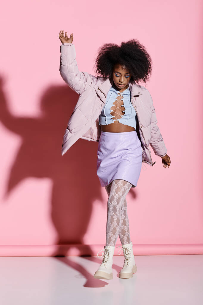カーリーヘアの若いアフリカ系アメリカ人女性は,活気に満ちたピンクの壁の前に自信を持って立って,彼女のスタイリッシュなスカートとジャケットアンサンブルを披露します. - 写真・画像