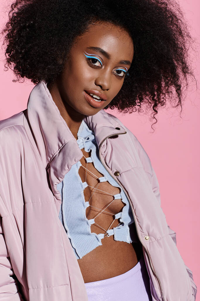 Стильна молода афроамериканка з кучерявим волоссям у рожевій куртці та синьою сорочкою в студійній обстановці. - Фото, зображення