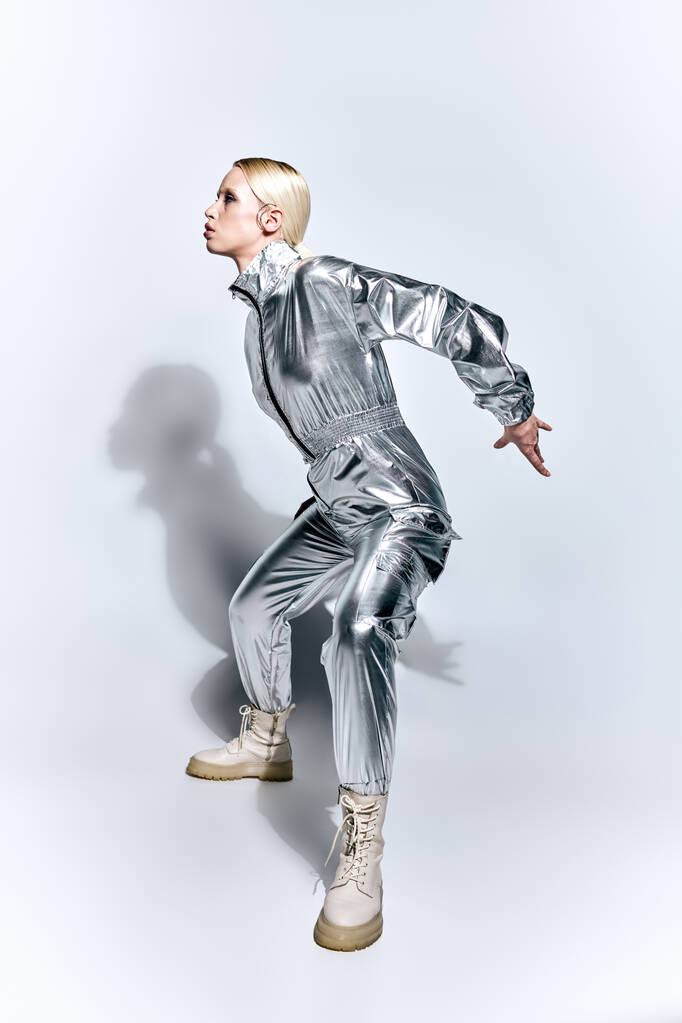 hermosa mujer en traje futurista plateado posando en movimiento sobre fondo gris y mirando hacia otro lado - Foto, imagen