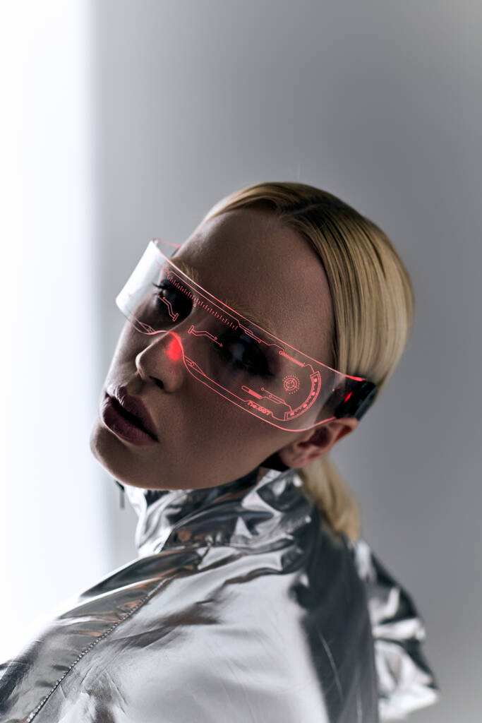 extraordinary woman with sci fi glasses in robotic clothing looking at camera on gray backdrop - Photo, Image