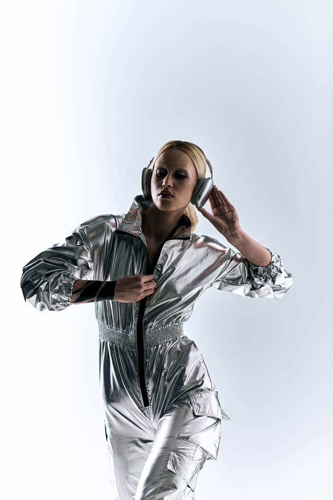 ekstrawagancki przystojny kobieta z nowoczesnych słuchawek w futurystyczny srebrny strój cieszący się muzyką - Zdjęcie, obraz