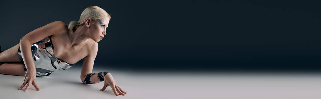 ekstrawagancka kobieta w srebrnym futurystycznym stroju leżąca na podłodze odwracając wzrok na czarnym tle, sztandar - Zdjęcie, obraz