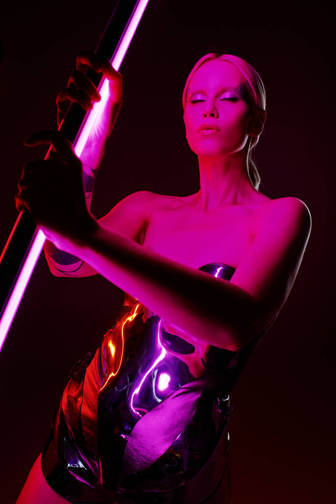 Metalik fütüristik giyimli, üzerinde parlak pembe LED lamba olan güzel görünümlü bir kadın modeli. - Fotoğraf, Görsel
