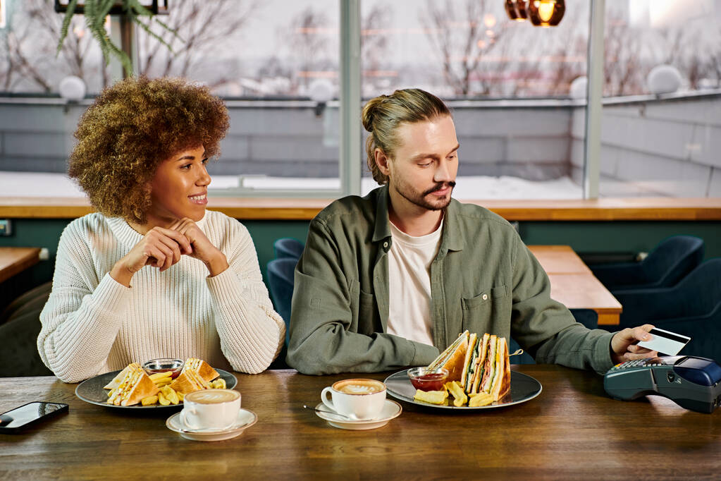 Eine afroamerikanische Frau und ein Mann sitzen an einem Tisch und genießen gemeinsam eine Mahlzeit in einem modernen Café. - Foto, Bild