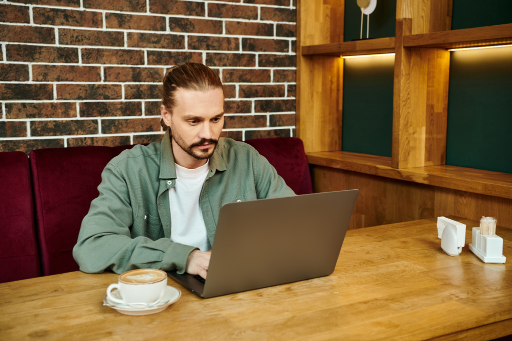 Чоловік працює на портативному комп'ютері за столом у сучасному кафе. - Фото, зображення