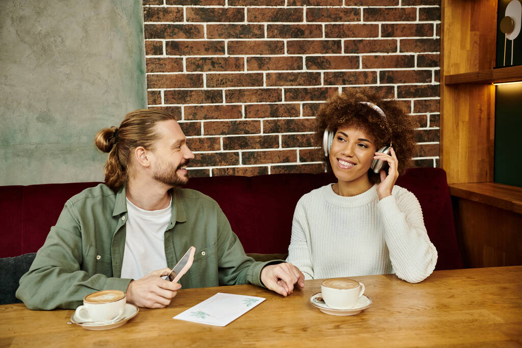 Een man en vrouw gaan in een levendige discussie terwijl ze aan een tafel zitten, beide verzonken in hun apparaten - Foto, afbeelding