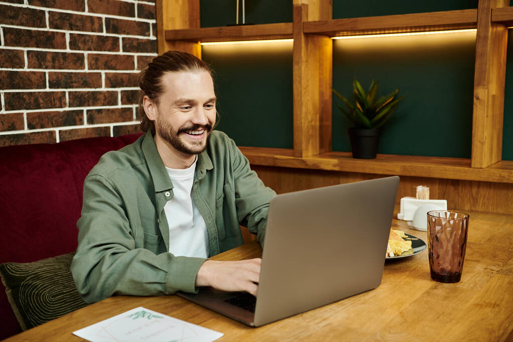 Чоловік інтенсивно зосереджений, використовує ноутбук за столом в сучасному кафе. - Фото, зображення