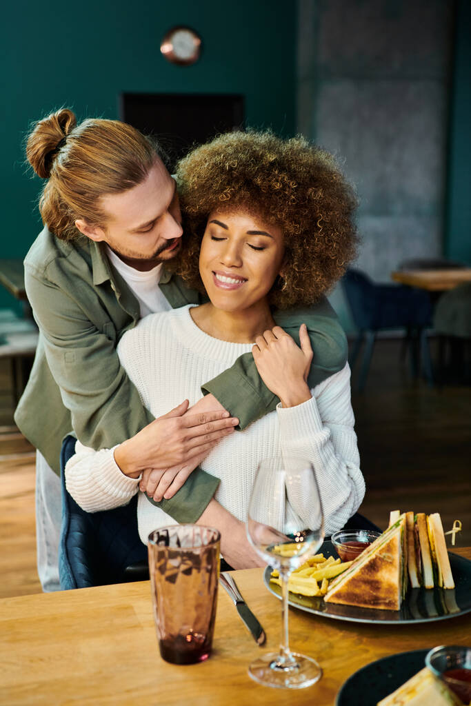 Een Afro-Amerikaanse vrouw en een man delen een oprechte knuffel aan een tafel in een modern café, die liefde en verbondenheid uitdrukken.. - Foto, afbeelding