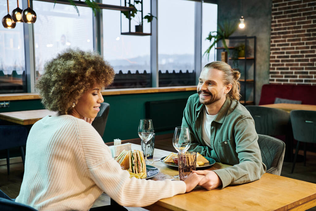 Uma mulher afro-americana e um homem desfrutando de uma refeição em um café moderno, envolvido em conversa e riso. - Foto, Imagem