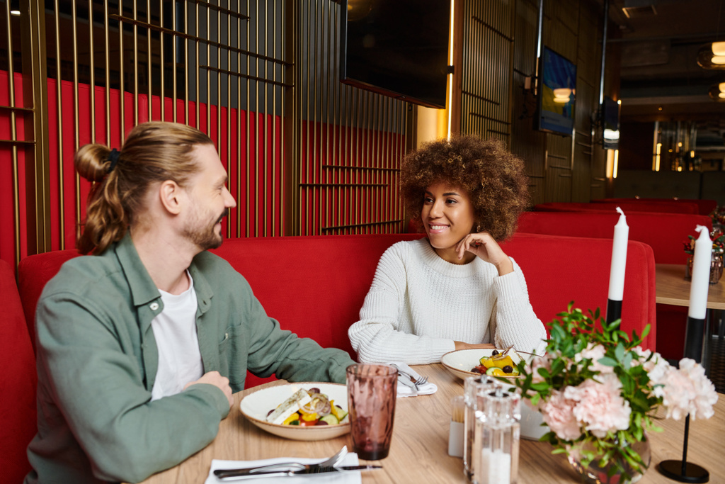 アフリカ系アメリカ人女性と男性がスタイリッシュなレストランテーブルで一緒に食事を楽しむ. - 写真・画像