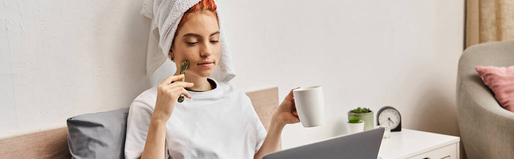 hermosa persona queer con toalla de pelo y rodillo de la cara beber té mientras mira películas, pancarta - Foto, Imagen