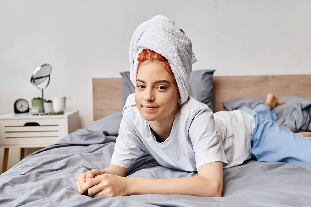 χαρούμενη όμορφη queer πρόσωπο με πετσέτα μαλλιών ψύξη στο κρεβάτι της και χαμογελώντας στην κάμερα, το πρωί - Φωτογραφία, εικόνα