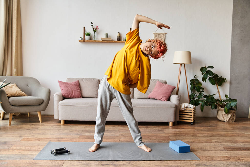 Хорошо выглядящий веселый странный человек в повседневной одежде активно упражняясь на коврике йоги в то время как дома - Фото, изображение